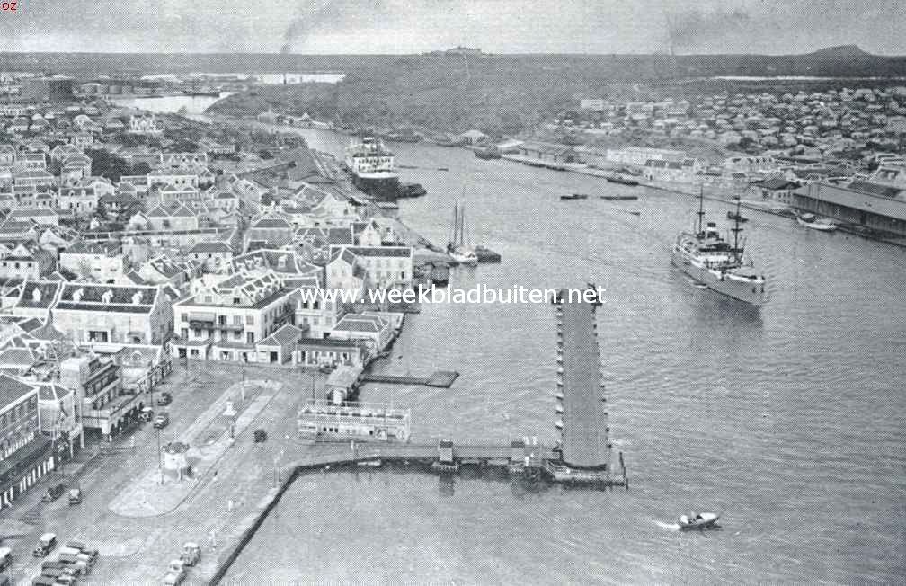 Curaao voorheen en thans. Curaao, de haven van Willemstad. Op den voorgrond de geopende pontonbrug, de koningin Emmabrug, die de twee helften der stad verbindt. Rechts het Brionplein en een gedeelte van Otrabanda (de overzijde). Op den achtergrond in het midden fort Nassau