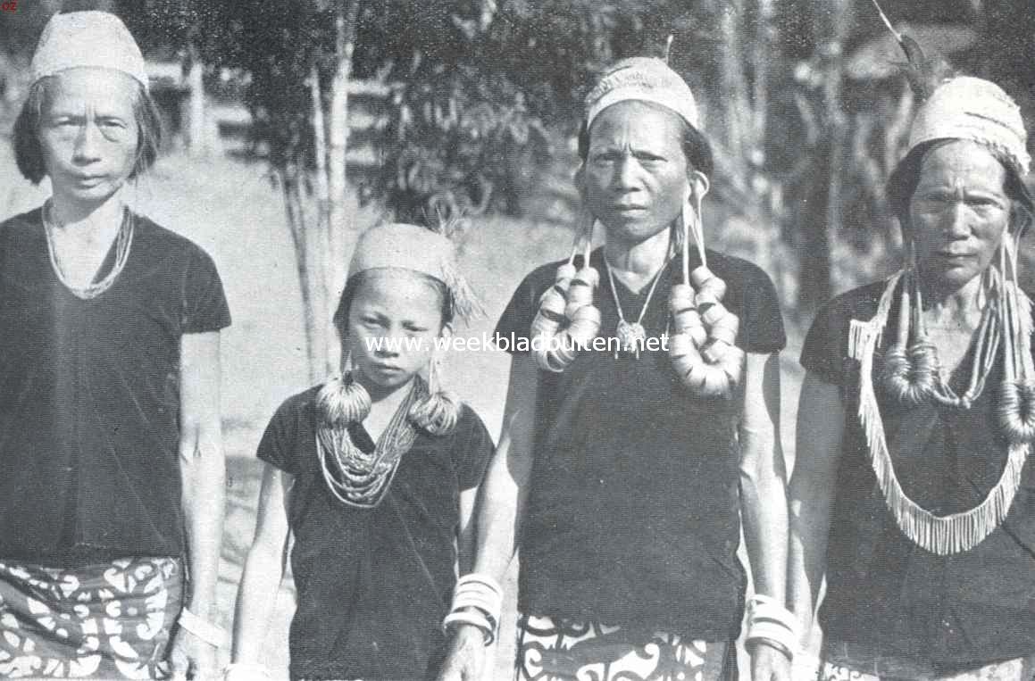 Het toilet der Apo-Kajans van Centraal Borneo. Vrouwen der Apo-Kajans in ouderwetsche kleeding, waarop drakenfiguren. Duidelijk zichtbaar zijn de lange oorlellen, die bij de vrouw links op de foto doorgescheurd zijn. Dit schoonheidsgebrek wordt gecamoufleerd, door met de haren de ooren te verbergen