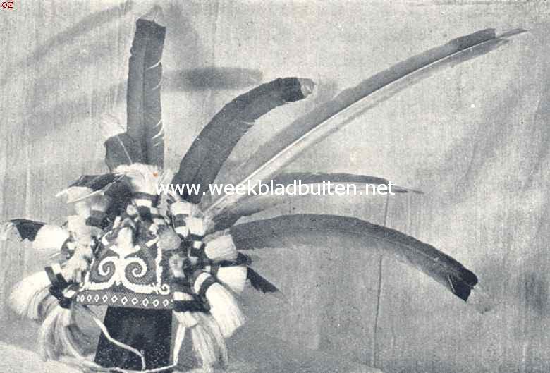 Dajaksche krijgshoed. Gemaakt van gevlochten rottans, versierd met de kostbare lange staartveeren van den magisch krachtigen neushoornvogel (de veeren zijn snellerattributen). De figuren in het kralenwerk hebben eveneens magische beteekenis